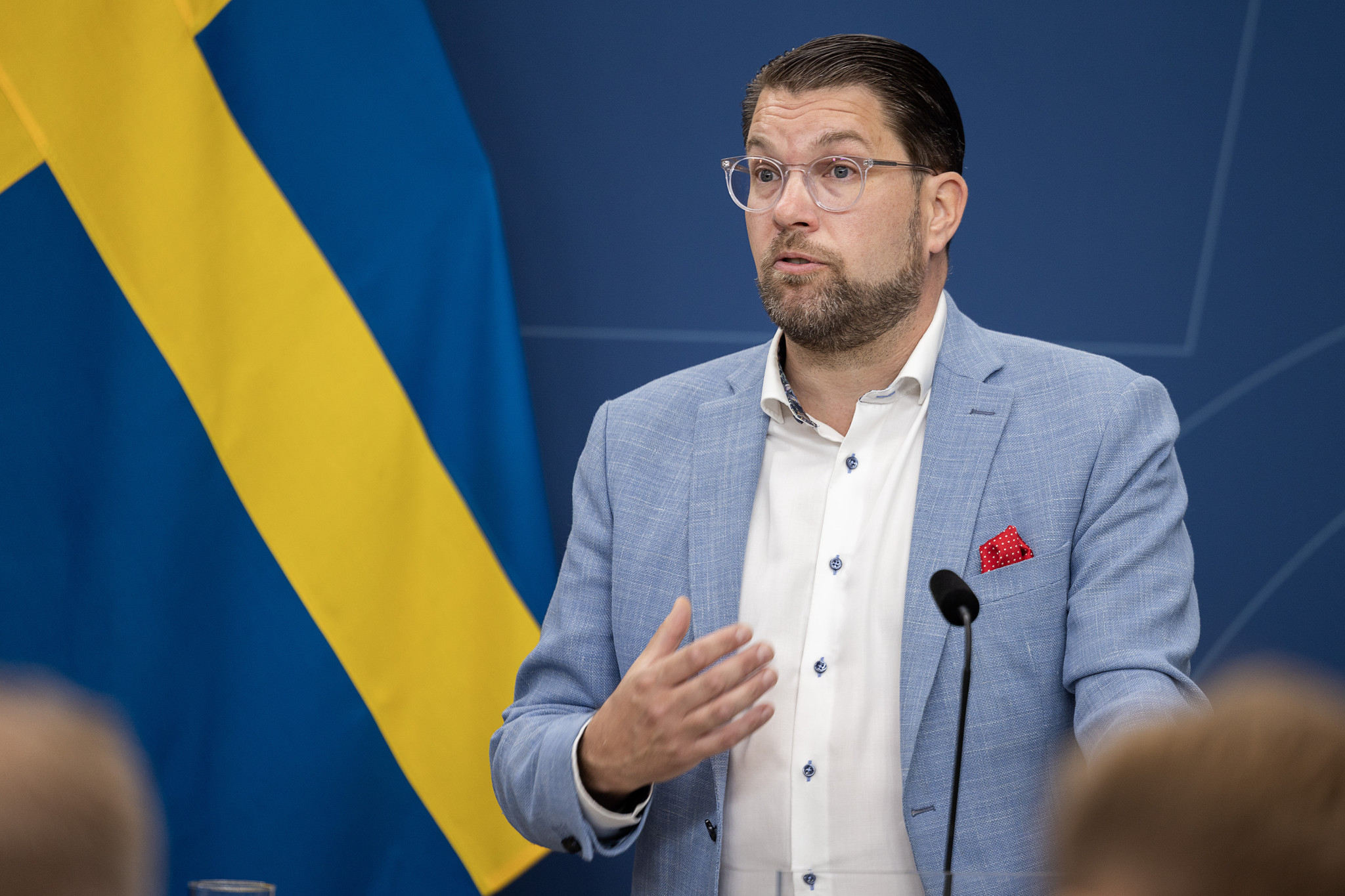 Sverigedemokraternas partiledare Jimmie Åkesson står i en talarstol framför svenska och eu-flaggor